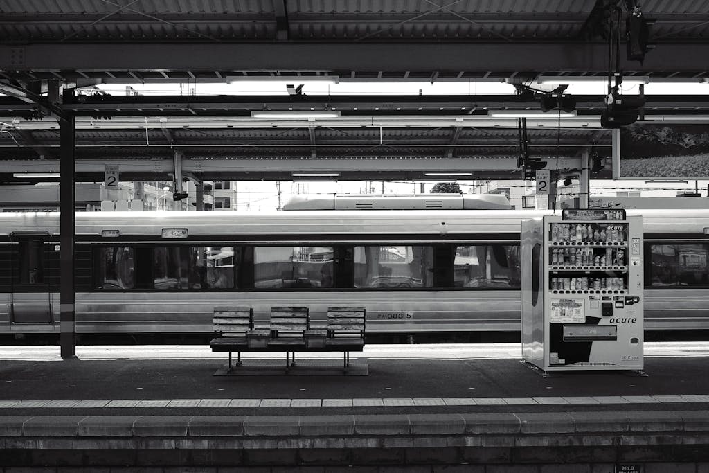 Black and white photo of a Nagano train station with vending machine and benches.